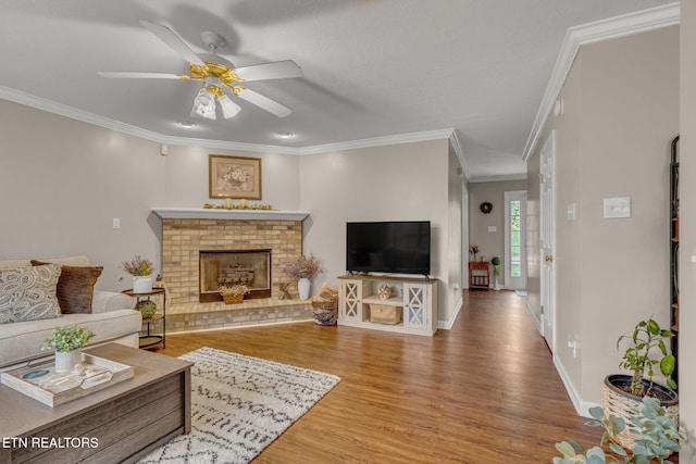 living room featuring wood finished floors, ceiling fan, crown molding, a brick fireplace, and baseboards