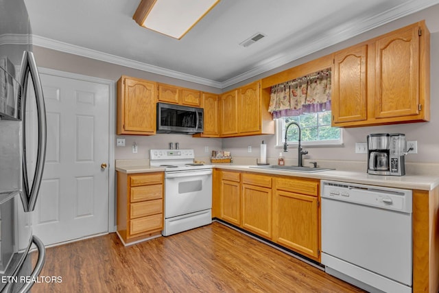 kitchen featuring stainless steel appliances, a sink, light countertops, light wood-type flooring, and ornamental molding