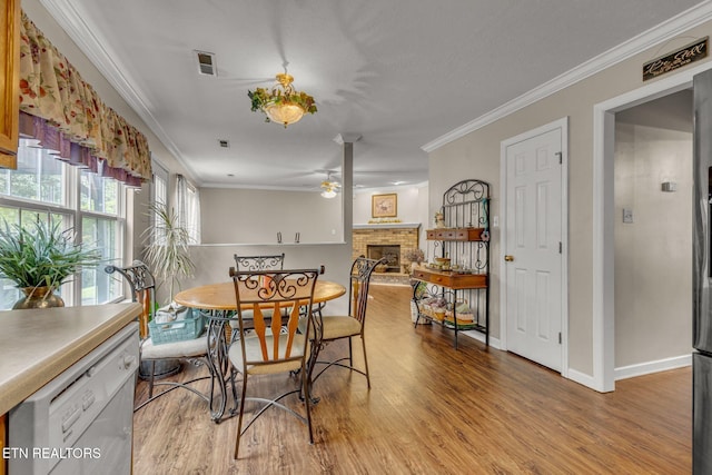 dining room with ceiling fan, light wood finished floors, a fireplace, crown molding, and baseboards