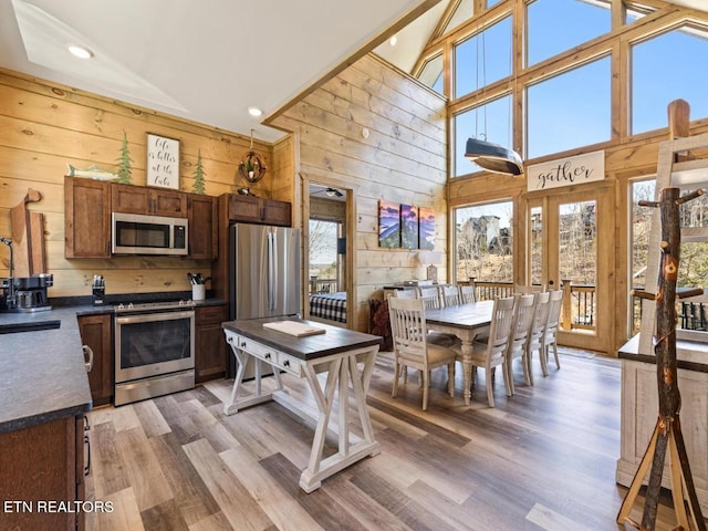 kitchen with appliances with stainless steel finishes, wood walls, high vaulted ceiling, dark countertops, and light wood-style floors