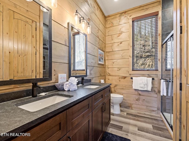 full bathroom featuring toilet, a stall shower, wood finished floors, wood walls, and double vanity
