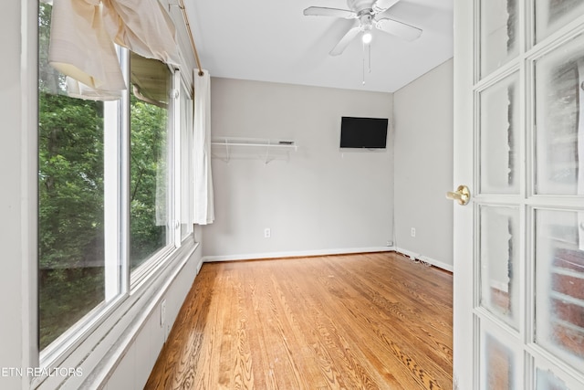 empty room featuring healthy amount of natural light, wood finished floors, baseboards, and ceiling fan