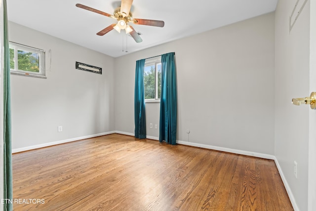 unfurnished room featuring plenty of natural light, wood finished floors, ceiling fan, and baseboards