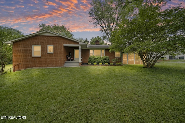 view of front of property featuring brick siding, a chimney, and a yard