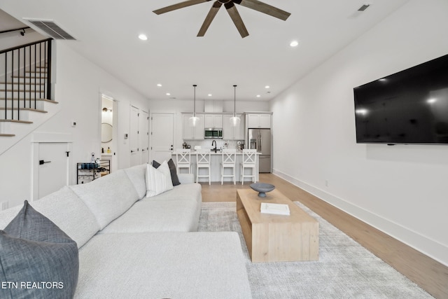 living room with ceiling fan, light wood-style flooring, baseboards, stairs, and recessed lighting