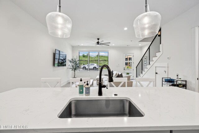 kitchen featuring a sink, open floor plan, light stone countertops, pendant lighting, and recessed lighting