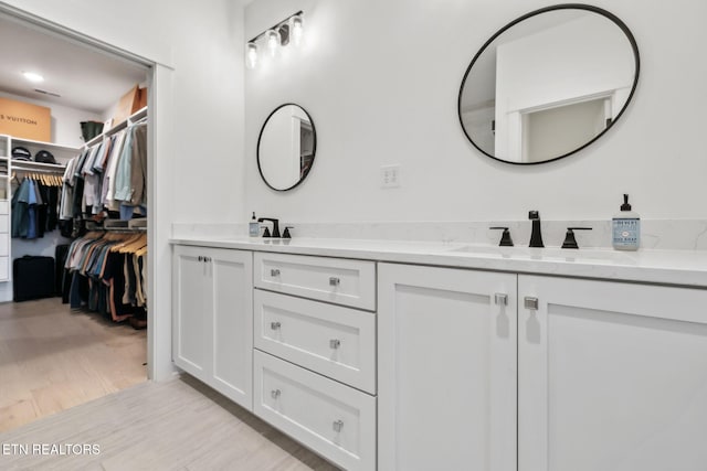 full bath featuring double vanity, a walk in closet, and wood finished floors