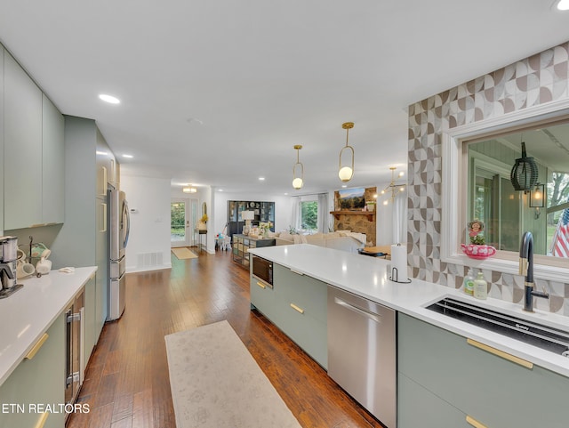 kitchen featuring appliances with stainless steel finishes, open floor plan, a sink, light countertops, and dark wood-type flooring