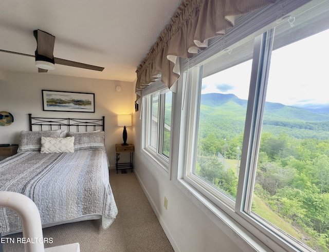 carpeted bedroom featuring baseboards, ceiling fan, a mountain view, and a forest view