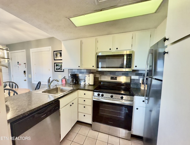 kitchen with appliances with stainless steel finishes, a sink, a peninsula, dark countertops, and light tile patterned floors