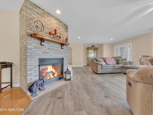 living room with light wood finished floors, a brick fireplace, baseboards, and recessed lighting