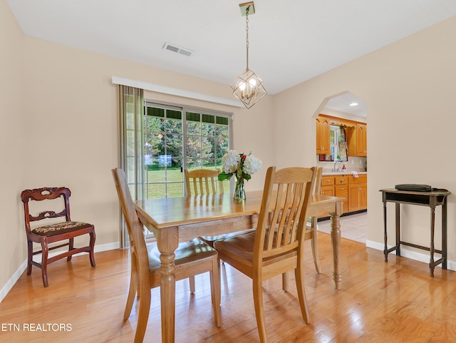 dining space with arched walkways, light wood-type flooring, baseboards, recessed lighting, and a chandelier