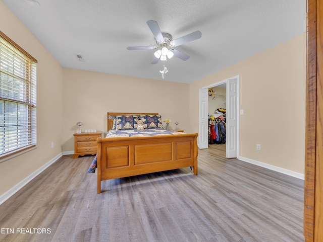 bedroom with light wood-type flooring, baseboards, and a spacious closet