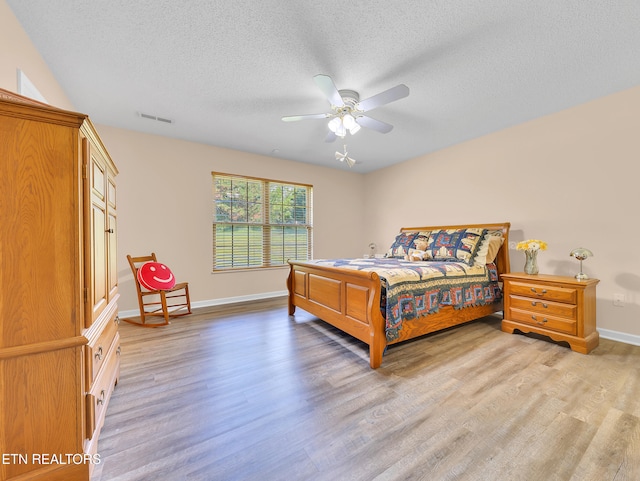 bedroom with light wood-style flooring, a textured ceiling, baseboards, and ceiling fan