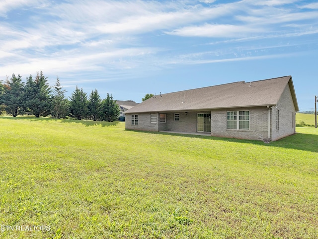 rear view of property featuring brick siding, a yard, and roof with shingles