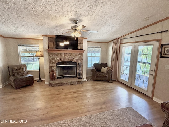 living room featuring crown molding, ceiling fan, wood finished floors, a stone fireplace, and baseboards