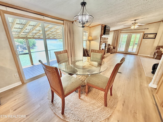 dining space with light wood-style floors, a textured ceiling, baseboards, a fireplace, and ceiling fan