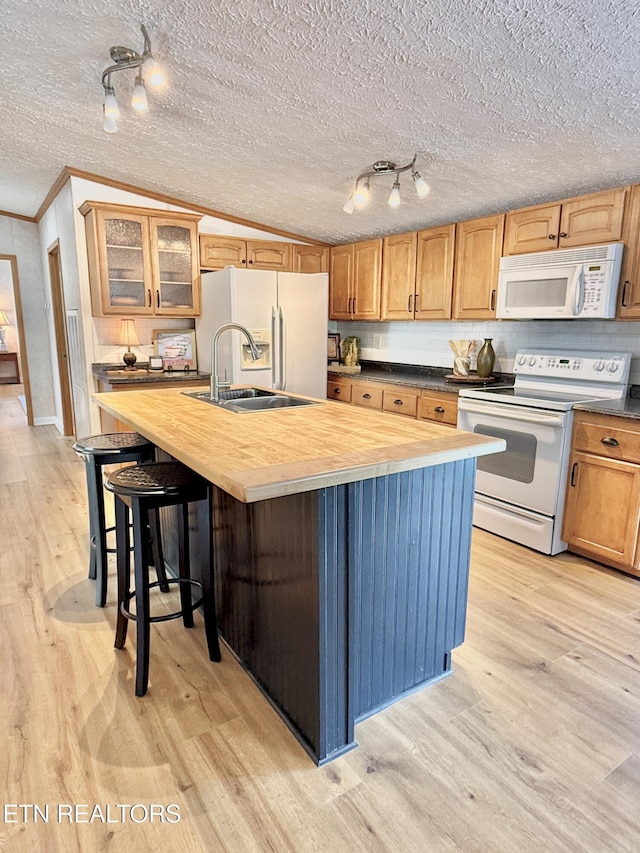 kitchen with white appliances, light wood-type flooring, ornamental molding, a kitchen island with sink, and wood counters