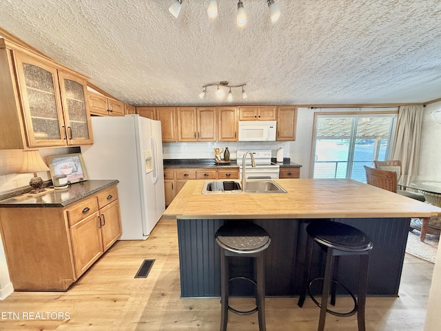 kitchen with white appliances, a sink, an island with sink, backsplash, and light wood-style floors