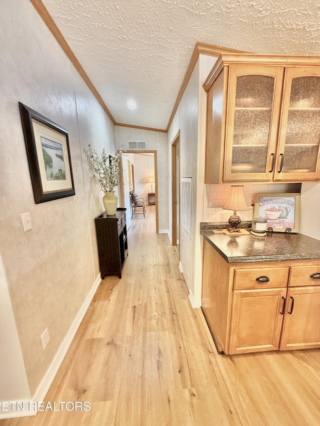hallway featuring crown molding, light wood-style floors, a textured ceiling, and baseboards