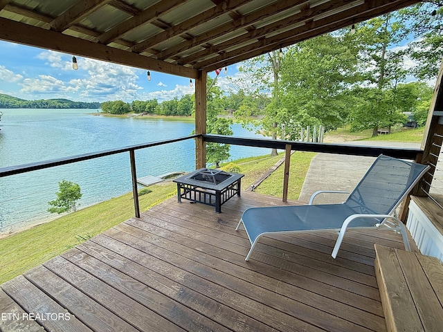 wooden terrace featuring a fire pit, a water view, and a lawn