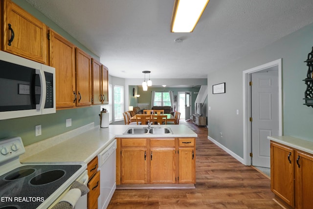 kitchen with white appliances, a peninsula, a sink, dark wood-type flooring, and light countertops