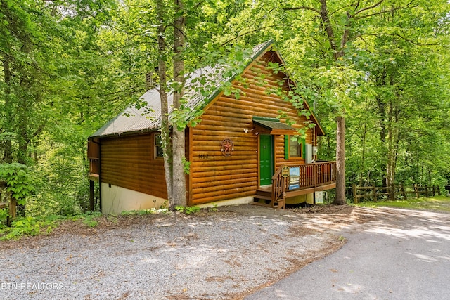 view of front of house with log veneer siding, metal roof, a view of trees, and a deck