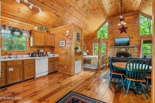 kitchen featuring white dishwasher, a sink, lofted ceiling, light wood finished floors, and wood walls