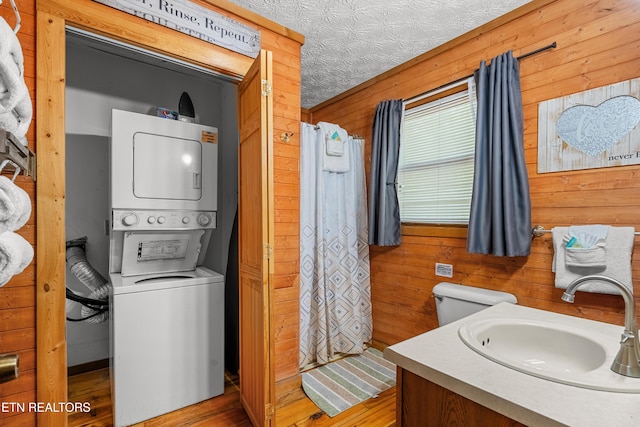 bathroom featuring stacked washer / dryer, wood walls, wood finished floors, curtained shower, and toilet