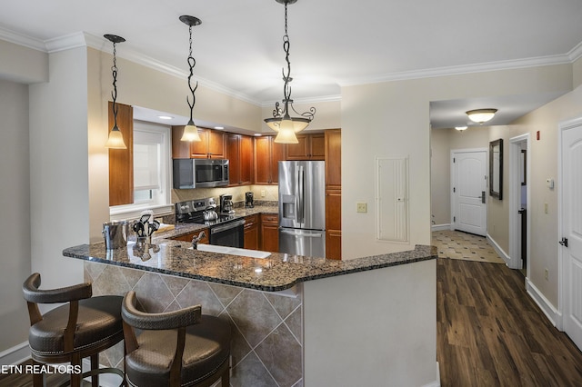 kitchen with appliances with stainless steel finishes, brown cabinetry, a peninsula, crown molding, and dark stone counters