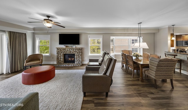 living room featuring ornamental molding, a ceiling fan, dark wood-type flooring, a fireplace, and baseboards