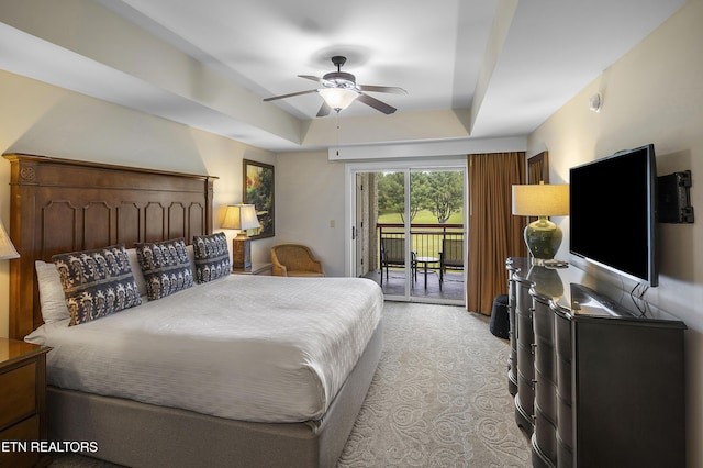 bedroom featuring access to exterior, a tray ceiling, light colored carpet, and a ceiling fan