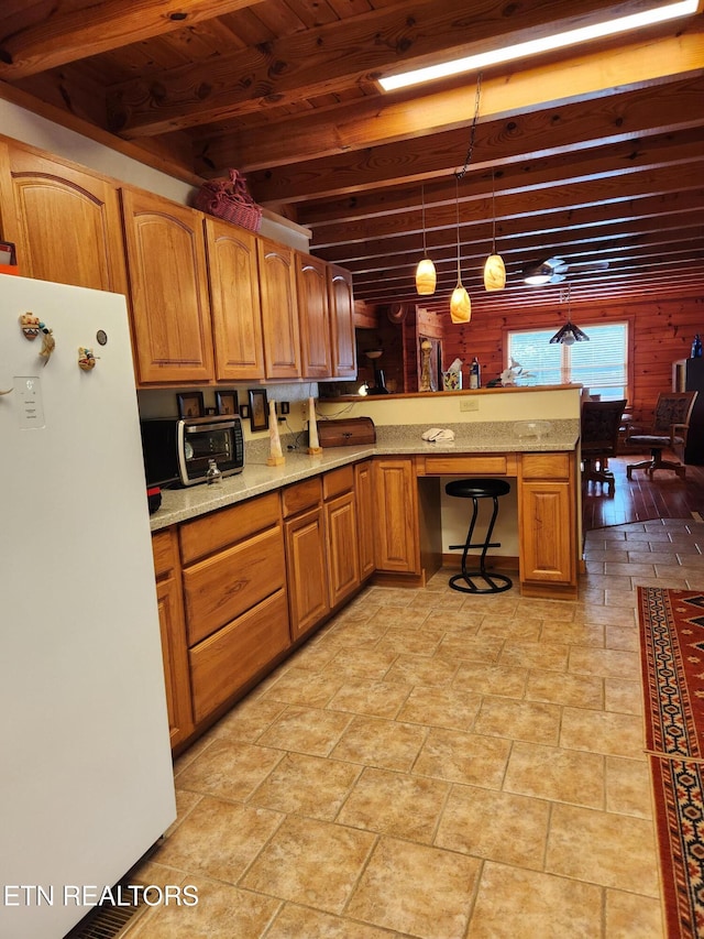 kitchen featuring freestanding refrigerator, brown cabinetry, a peninsula, decorative light fixtures, and light stone countertops