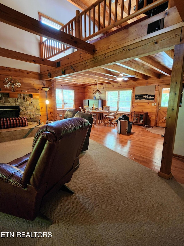 living area with wooden walls, healthy amount of natural light, wood finished floors, a stone fireplace, and beamed ceiling