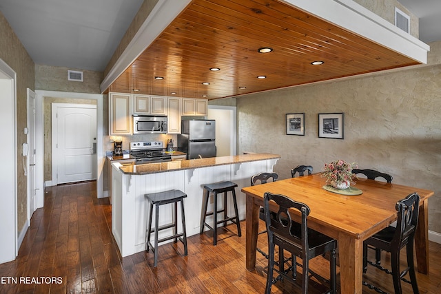 kitchen featuring appliances with stainless steel finishes, dark wood finished floors, a breakfast bar area, recessed lighting, and dark stone counters