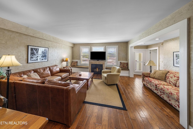 living room featuring wallpapered walls, hardwood / wood-style floors, and a warm lit fireplace