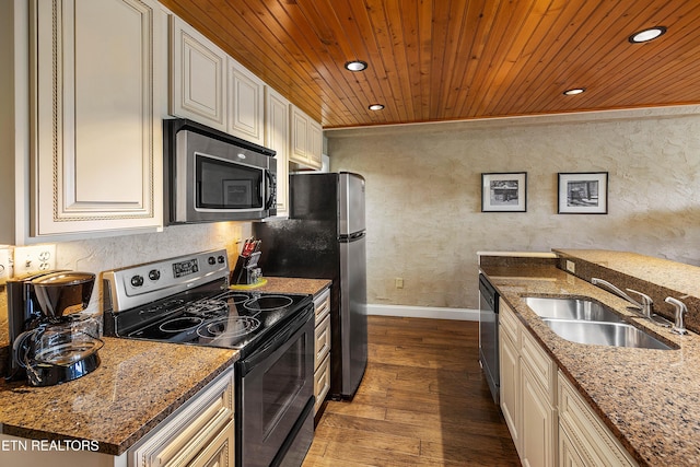 kitchen featuring appliances with stainless steel finishes, a sink, baseboards, cream cabinets, and a textured wall