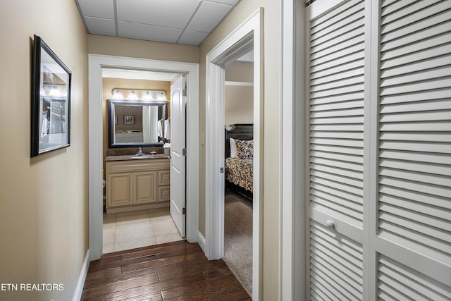 hallway featuring dark wood finished floors, baseboards, a paneled ceiling, and a sink