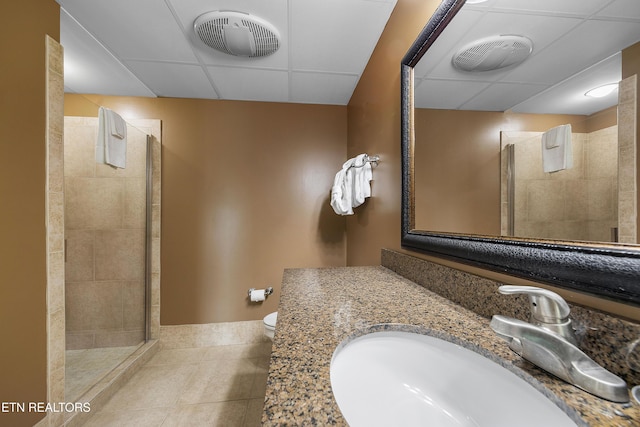 full bathroom with baseboards, tile patterned flooring, tiled shower, a paneled ceiling, and toilet