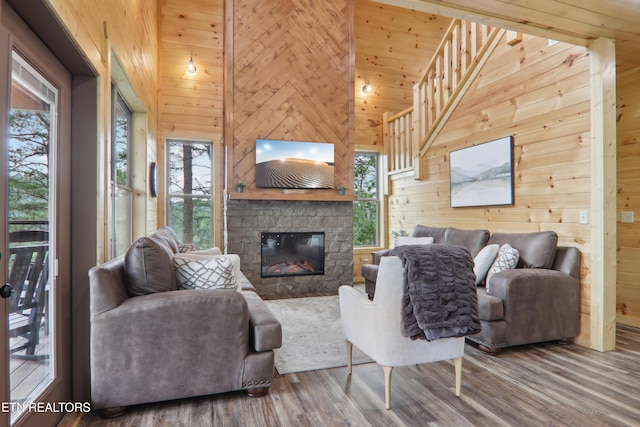 living area featuring wooden walls, wood finished floors, plenty of natural light, a fireplace, and a high ceiling