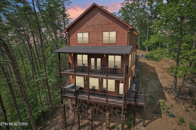 back of house at dusk featuring a balcony, french doors, stairway, and a deck