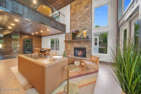 living area featuring a stone fireplace, wooden ceiling, a high ceiling, and wood finished floors