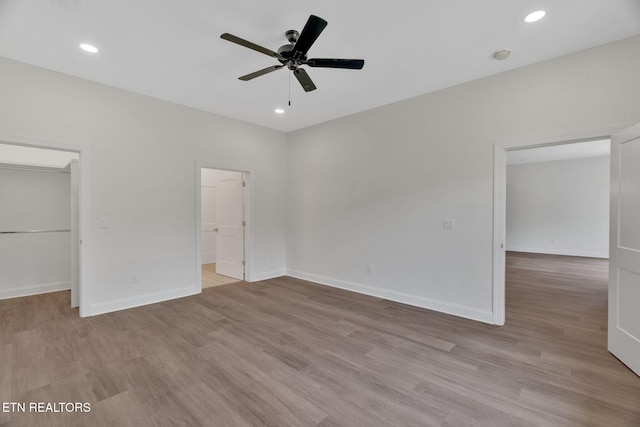 unfurnished bedroom featuring a walk in closet, wood finished floors, baseboards, recessed lighting, and a closet