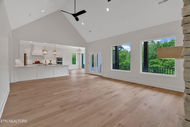 unfurnished living room featuring high vaulted ceiling, plenty of natural light, a ceiling fan, light wood finished floors, and baseboards