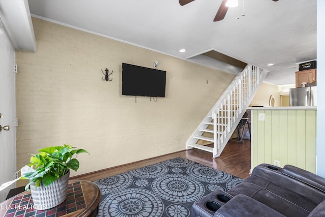 living area with wood finished floors, ceiling fan, baseboards, brick wall, and stairs