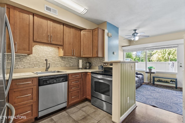kitchen featuring appliances with stainless steel finishes, a sink, a ceiling fan, light countertops, and brown cabinetry