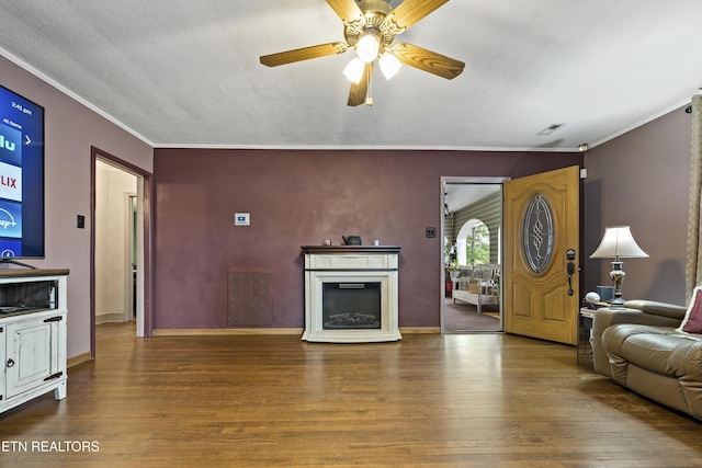living area with wood finished floors, crown molding, ceiling fan, a fireplace, and baseboards