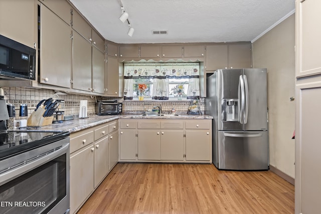 kitchen with stainless steel appliances, a sink, light wood finished floors, decorative backsplash, and light stone countertops