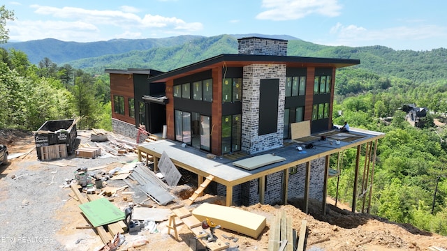 view of side of home with a wooded view, a mountain view, stone siding, and a chimney