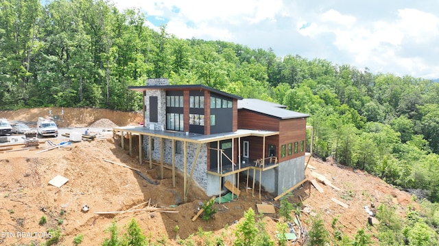 back of house with a wooded view and stone siding